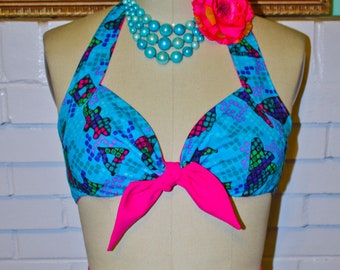 May include: A blue and pink two-piece swimsuit with a geometric fish pattern. The top has a halter style with a bow tie closure. The bottom is a high-waisted short.
