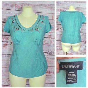 May include: A turquoise linen top with a V-neck and short sleeves. The neckline and upper chest feature embroidered detailing. The tag reads "LANE BRYANT" and size 14/16. The fabric is 55% linen and 45% rayon.