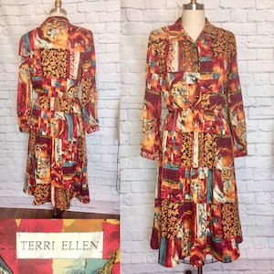 Op de afbeelding: Een lange mouwen jurk met een kleurrijke abstracte print in tinten rood, oranje, geel, blauw en groen. De jurk heeft een knoopsluiting aan de voorkant en een riem. Het label luidt "TERRI ELLEN".
