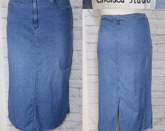 May include: A long denim skirt with a frayed hem and a center back slit. The skirt is a light blue wash and has a zipper closure. The label on the skirt reads "Chelsea Studio".