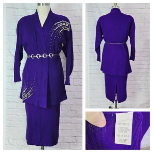May include: A purple knit sweater set with a skirt and a cardigan. The cardigan has a silver beaded design on the front. The label reads "100% Acrylic, Dry Clean Only, Made in U.S.A., One Size".