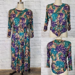 May include: A long-sleeved dress with a colorful abstract print in shades of teal, purple, brown, and white. The dress has a button-up front and a matching belt.