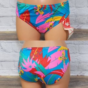 Pode incluir: Um par de calcinhas de biqu&iacute;ni vintage com uma estampa floral tropical vibrante. As calcinhas apresentam um fundo turquesa com desenhos de folhas e flores rosa, vermelhas, amarelas e verdes. Uma etiqueta "Cole" est&aacute; anexada.