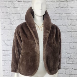 Könnte beinhalten: Eine braune Kunstfelljacke mit einem breiten Kragen. Die Jacke ist vorne offen und hat eine lockere Passform.