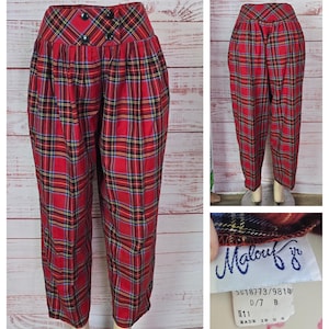 May include: Red plaid pants with a high waist and button details. The pants feature a classic tartan pattern in red, black, yellow, and blue. The tag reads "Malouf jr" and includes size information. The pants are displayed on a mannequin.