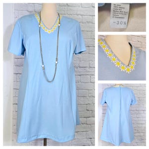 May include: A light blue short-sleeved dress with a daisy embroidered neckline. The dress has a v-neck and a slightly flared skirt. The dress is made of a soft, comfortable fabric and is perfect for a casual summer day. The dress is shown on a mannequin with a silver necklace.