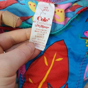 Pode incluir: Um fato de banho vintage colorido com um padr&atilde;o tropical em vermelho, azul, rosa e amarelo. A etiqueta diz "Cole of California Her Majesty" e indica o tamanho 14YJ. Fabricado nos EUA. O fato de banho tem um design colorido.