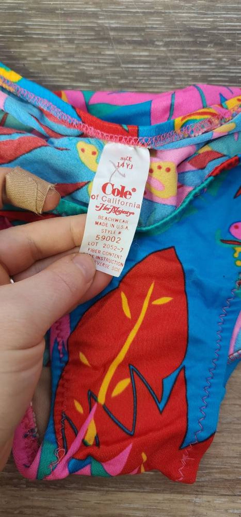 Pode incluir: Um fato de banho vintage colorido com um padr&atilde;o tropical em vermelho, azul, rosa e amarelo. A etiqueta diz "Cole of California Her Majesty" e indica o tamanho 14YJ. Fabricado nos EUA. O fato de banho tem um design colorido.