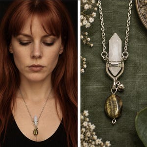 May include: A silver-toned necklace featuring a double-terminated clear quartz crystal point held in a metal setting, with a small silver bell charm and a smooth, oval-shaped brown and gold tiger's eye gemstone pendant hanging below the crystal.
