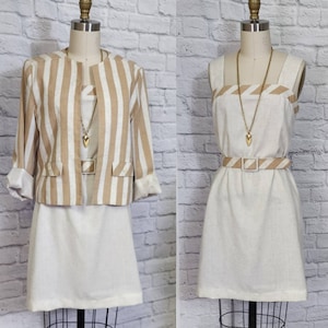May include: A two-piece outfit with a striped beige and white jacket and a matching white dress with a beige stripe detail. The dress has a gold chain necklace with a heart pendant and a beige belt.