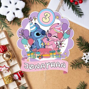 Może przedstawiać: Topper na tort urodzinowy z postaciami Stitch i Angel, z numerem 3. Topper ma r&oacute;żowy baner z napisem "JONATHAN". Projekt zawiera balony, prezenty i tort urodzinowy ze świeczkami.