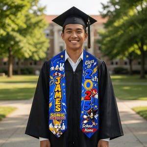 May include: A smiling graduate in a black cap and gown, wearing a blue Sonic the Hedgehog graduation stole. The stole features the name "JAMES", "Class of 2025", and Sonic characters. The school name is also visible.