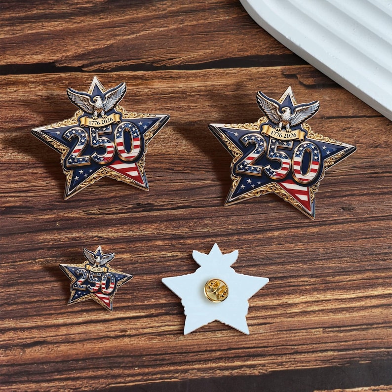 May include: Star-shaped pins with a patriotic design. The pins feature the number "250" in the centre, with red and white stripes and blue stars. An eagle and the text "1776-2026" are at the top. One pin is shown with the back exposed.