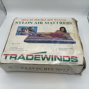 May include: A box for a Deluxe Double Box Waffle Nylon Air Mattress. The box is worn and shows the product's dimensions as 145 x 198 cm. The box has the Tradewinds logo and features an image of the mattress in use.