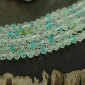 May include: A strand of faceted, clear glass beads with a light blue and green color gradient. The beads are round and have a slightly irregular shape.