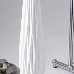May include: A tall, white ceramic vase with a geometric diamond pattern. The vase has a narrow neck and a wide base. The design features vertical and diagonal lines, creating a textured surface. The vase is a decorative home accent.