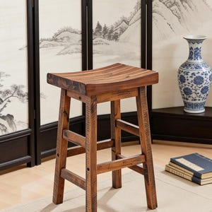 May include: A rustic wooden bar stool with a curved seat and four sturdy legs. The stool is made of dark brown wood with visible grain and a distressed finish. The design is simple and functional, suitable for a kitchen or bar setting.