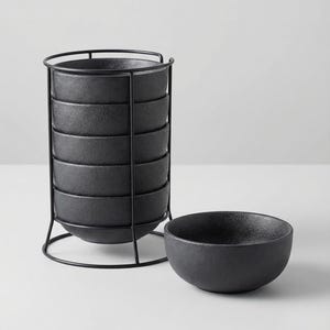 May include: A set of six black textured bowls, stacked in a black metal stand, with one bowl placed separately. The bowls have a matte finish and a simple, modern design. Ideal for serving snacks or small portions.