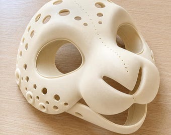May include: A cream-coloured, 3D-printed animal mask featuring a rounded snout, large eye openings, and a series of circular perforations across the forehead and sides. The surface displays a fine, layered texture consistent with additive manufacturing.