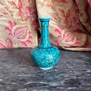 May include: A small turquoise vase with a narrow neck and a bulbous base, featuring intricate black line drawings of floral patterns and teardrop shapes covering the entire exterior surface of the ceramic vessel.