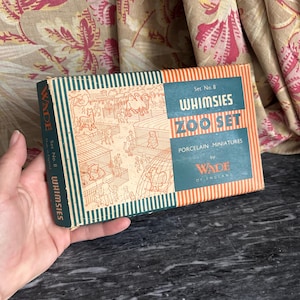 以下が含まれることがあります： 青緑色とオレンジ色のストライプ柄が特徴のWade Whimsies Zoo Set No. 8用長方形の紙箱。箱には動物園の線画イラストと「Set No. 8 WHIMSIES ZOO SET PORCELAIN MINIATURES by WADE OF ENGLAND」という文字が印刷されています。