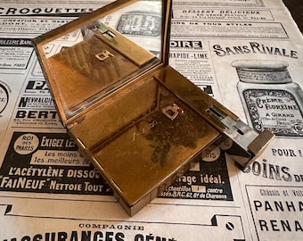 May include: A rectangular gold-toned metal compact case with an attached mirror on the inside lid. The surface features the embossed text Shiseido. A small metal sliding mechanism is visible on the right side of the base, extending outward.