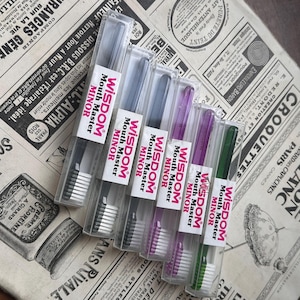May include: Several Wisdom Mouth Master Minor toothbrushes in transparent cases. The toothbrushes have coloured handles in black, grey, purple, and green, with white bristles. Each case features a label with the product name.
