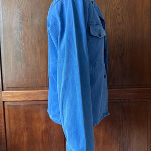 May include: A bright blue long-sleeved jacket featuring a collared neckline, a button-down front, and a single chest pocket. The garment is displayed on a mannequin and has a raw, frayed hemline at the bottom of the sleeves and the torso.