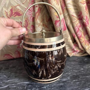 May include: A barrel-shaped ice bucket with a dark brown and white marbled glaze finish. It features a metallic lid with a small central knob and a matching arched metal handle. The body is accented with two horizontal cream-coloured bands.