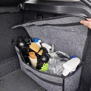 May include: A gray felt car organizer filled with various car cleaning supplies. The organizer is open, revealing black bottles, spray bottles, brushes, and microfiber cloths. The organizer is in the trunk of a car.