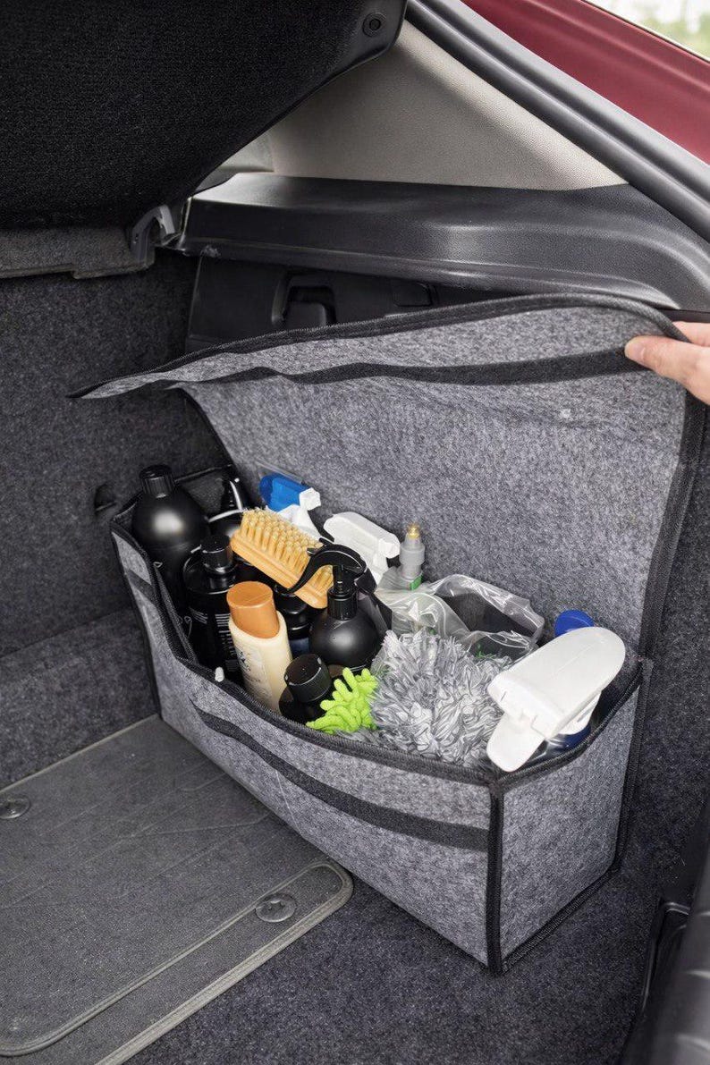 May include: A gray felt car organizer filled with various car cleaning supplies. The organizer is open, revealing black bottles, spray bottles, brushes, and microfiber cloths. The organizer is in the trunk of a car.