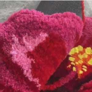 May include: Close-up of a vibrant, textured floral design. The petals are a deep red, transitioning to a lighter pink with white accents. Yellow and orange details form the flower's center, creating a striking contrast.