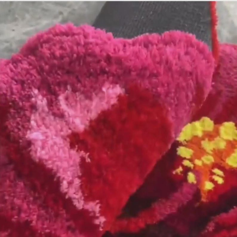 May include: Close-up of a vibrant, textured floral design. The petals are a deep red, transitioning to a lighter pink with white accents. Yellow and orange details form the flower's center, creating a striking contrast.