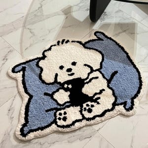 May include: A white and blue rug in the shape of a cartoon dog. The dog is white with black accents, and the rug has a light blue background. The rug is placed on a white marble floor.