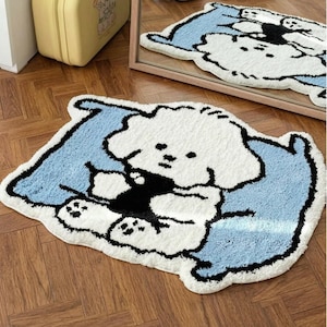 May include: A plush, cartoon-style rug featuring a white dog-like character on a light blue background. The rug has a black outline and is placed on a wooden floor. The rug's design is also reflected in a nearby mirror.