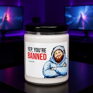 CaseOh Yep You're Banned candle on a gaming desk in a purple-lit room, 12 oz paraffin candle in a glass jar with a black lid