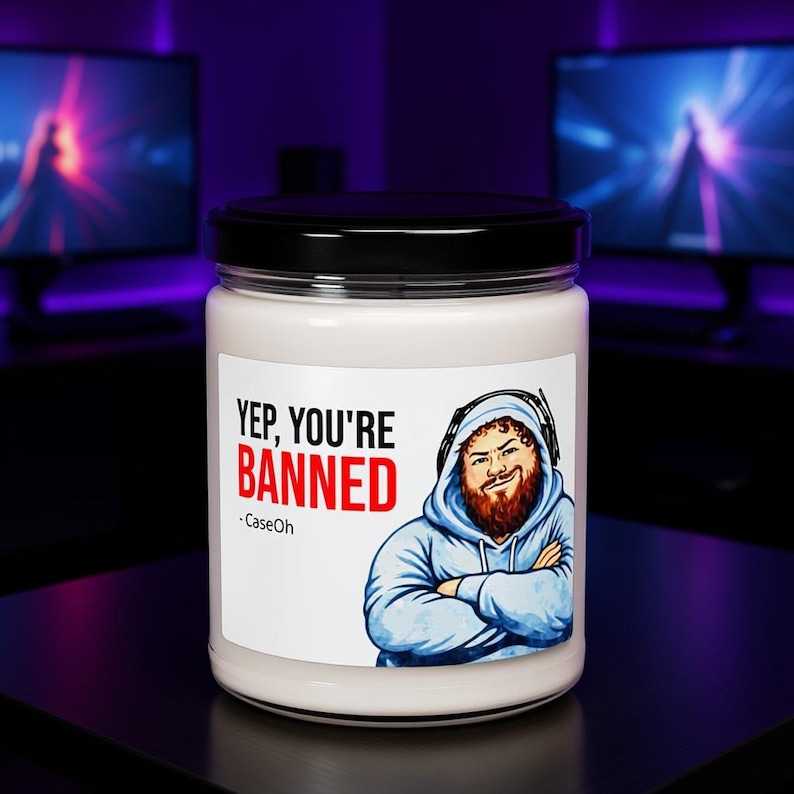 CaseOh Yep You're Banned candle on a gaming desk in a purple-lit room, 12 oz paraffin candle in a glass jar with a black lid