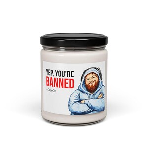 CaseOh Yep You're Banned candle, 12 oz paraffin meme candle in a glass jar with a black lid, front view on white