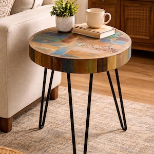 May include: A round side table with a multi-colored, reclaimed wood top and black hairpin legs. The table is topped with a small potted plant, a book, and a beige mug. The table is approximately 20 inches in diameter.