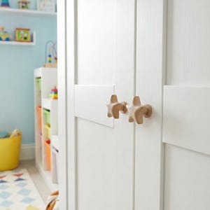 May include: White wooden closet doors with star-shaped knobs. The knobs are made of light-colored wood. The closet doors are part of a child's room, with toys and shelves visible in the background.
