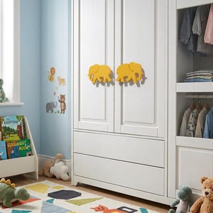 Peut inclure: Une armoire en bois blanc dotée de deux boutons de porte en forme d'éléphant jaune. L'armoire comporte deux tiroirs inférieurs et une section latérale ouverte avec des vêtements suspendus. La pièce contient un porte-livres, un tapis et des peluches.