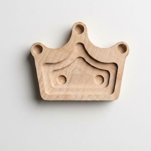 May include: A wooden crown-shaped tray with a natural finish. The tray features a layered design with rounded cutouts, including three circular indentations at the top and two at the base, creating a decorative and functional piece.