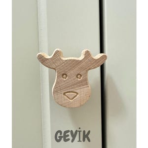 May include: A wooden cabinet knob in the shape of a reindeer head. The knob is light brown and has a simple design with two eye holes and a mouth. The word "GEYIK" is written below the knob.