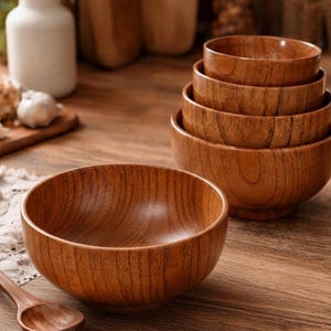Puede incluir: Conjunto de cuencos de madera de diferentes tama&ntilde;os, apilados y dispuestos sobre una superficie de madera. Los cuencos tienen un acabado de veta de madera natural y est&aacute;n vac&iacute;os. Una cuchara de madera descansa cerca, sugiriendo un entorno de cocina o comedor.