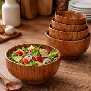 Puede incluir: Un juego de cuencos de ensalada de madera de diferentes tama&ntilde;os, apilados y colocados sobre una superficie de madera. Un cuenco est&aacute; lleno de una ensalada fresca con tomates, pepinos y cebollas rojas. Una cuchara de madera est&aacute; cerca. Los cuencos tienen un acabado de veta de madera natural.