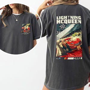 Puede incluir: Camiseta gris oscuro con Lightning McQueen de la pel&iacute;cula Cars. La parte trasera muestra un gr&aacute;fico del coche de carreras rojo con el n&uacute;mero 95, banderas a cuadros y el texto "Lightning McQueen". La parte delantera tiene un gr&aacute;fico m&aacute;s peque&ntilde;o.