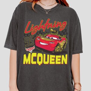 Puede incluir: Camiseta gris oscuro con un dise&ntilde;o de Rayo McQueen de la pel&iacute;cula Cars. El dise&ntilde;o incluye los textos "Lightning", "95" y "McQueen" en amarillo y rojo.