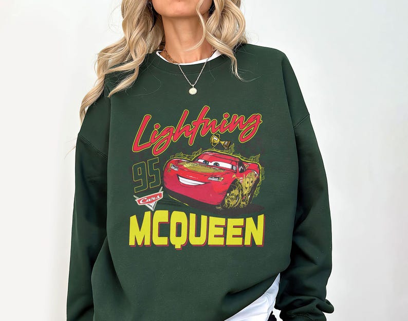 Puede incluir: Sudadera verde oscuro con un gr&aacute;fico de Rayo McQueen de la pel&iacute;cula Cars. El dise&ntilde;o incluye el texto "Lightning McQueen", el n&uacute;mero "95" y el nombre "McQueen" en amarillo. El gr&aacute;fico es en rojo, amarillo y verde.