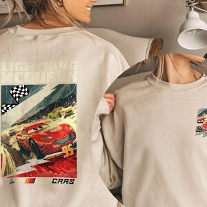 Puede incluir: Sudadera beige con un gr&aacute;fico de Rayo McQueen de la pel&iacute;cula Cars. El gr&aacute;fico frontal muestra una escena de carrera con el n&uacute;mero 95. La parte posterior de la sudadera tiene un gr&aacute;fico m&aacute;s peque&ntilde;o del n&uacute;mero 95.