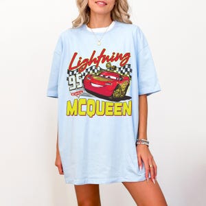 Puede incluir: Camiseta azul claro con un dise&ntilde;o de Rayo McQueen de la pel&iacute;cula Cars. El dise&ntilde;o incluye el texto "Lightning McQueen", "95" y "Cars" en rojo y amarillo. La camiseta tiene mangas cortas y cuello redondo.